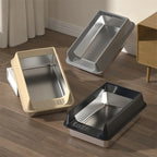 Trois bacs à litière en inox pour chat avec rebords beige, gris et noir sur un parquet.